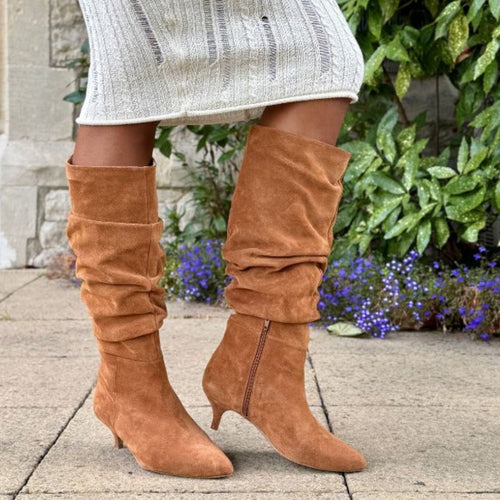 Brown wide fit knee-high boots worn with a light-colored dress against a garden background.